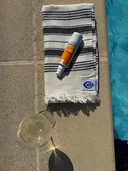  Peshtemal La Perle Lys en coton turc rayé au bord d'une piscine avec crème solaire et verre de vin blanc
